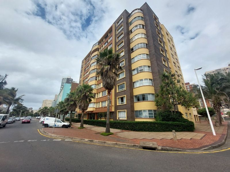 A street-level view of a multi-story apartment building featuring a curved facade, brick and painted exterior finishes, and surrounding paved sidewalk.