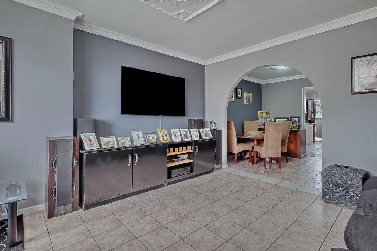 A living room featuring tiled flooring, decorative ceiling cornices, and an arched entryway leading to the dining area.