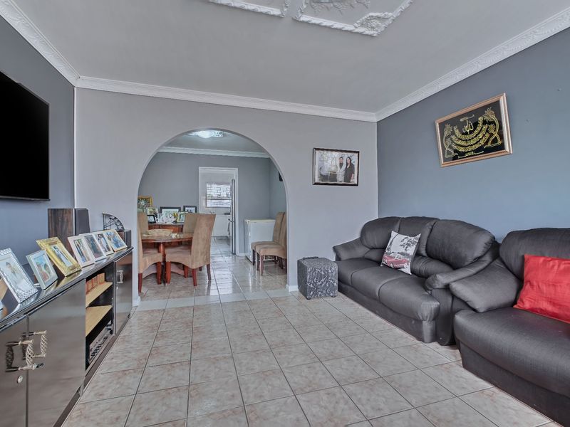 A living room featuring tiled flooring, decorative ceiling cornices, and an arched entryway leading to an adjacent dining area.