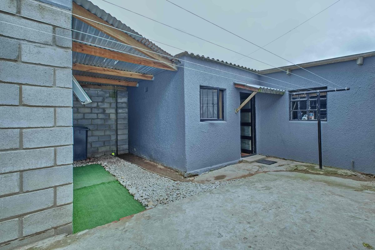 Rear exterior view showing a concrete paved courtyard, textured wall finishes, and a covered utility area with exposed blockwork and corrugated roofing.