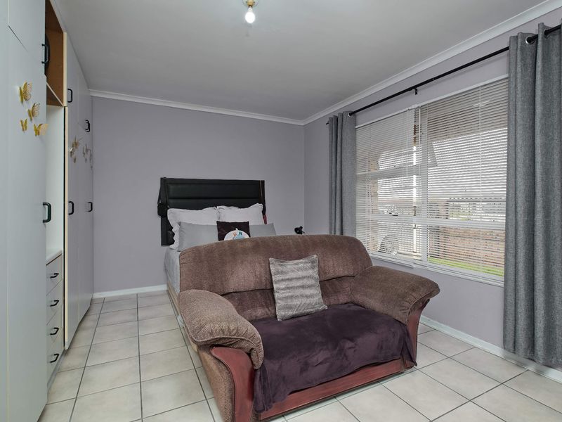 A bedroom featuring tiled flooring, built-in cupboards, and large windows with venetian blinds and curtain rails.