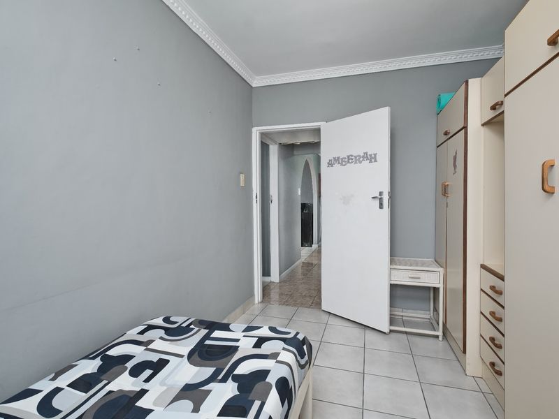 A bedroom featuring tiled flooring, built-in cupboards, and neutral wall paint, offering a functional space with potential for cosmetic updates.