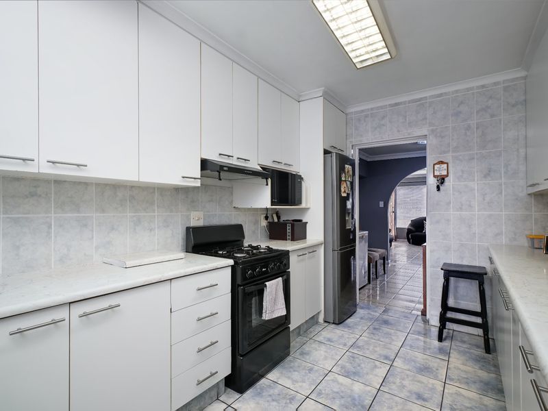 A functional kitchen featuring white cabinetry, laminate countertops, a gas stove with extractor fan, and tiled finishes throughout.