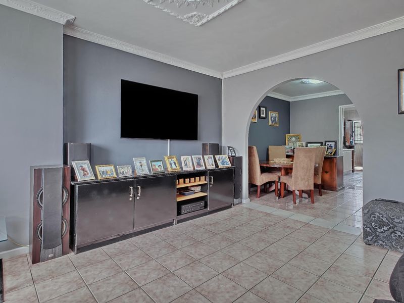A living room featuring tiled flooring, decorative ceiling cornices, and an arched entryway leading to the dining area.