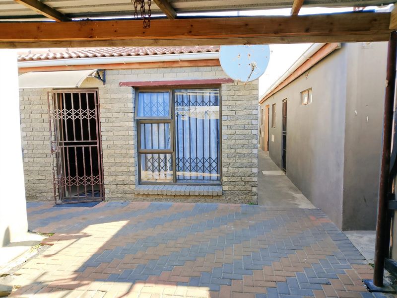 A paved outdoor patio area featuring a covered structure, security gate, and aluminium window frames, providing access to the side of the property.