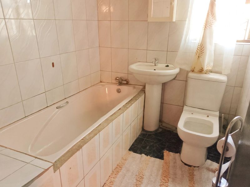 A functional bathroom featuring a pedestal washbasin, built-in bathtub, and toilet, finished with ceramic wall and floor tiling.