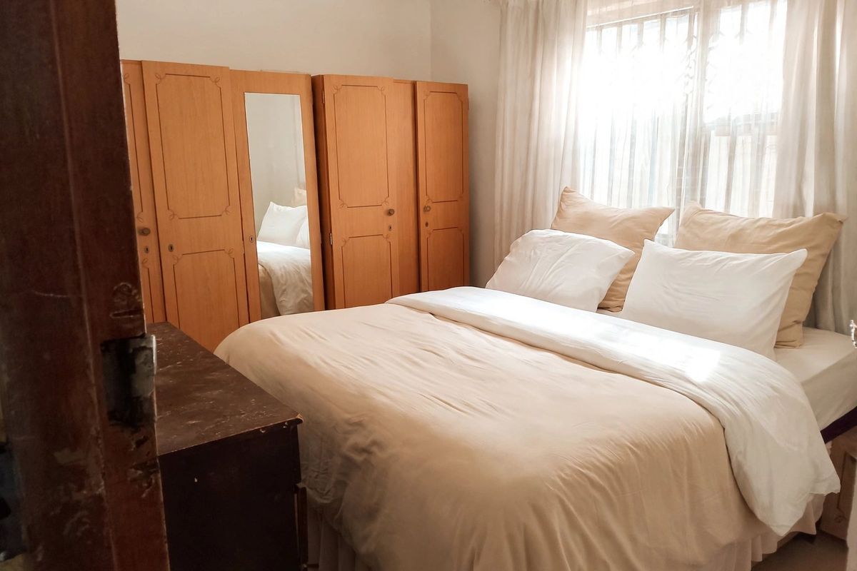 A bedroom featuring built-in wooden cupboards and a window with security bars, offering a functional space with natural light.