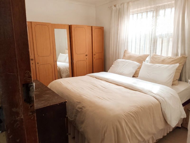 A bedroom featuring built-in wooden cupboards and a window with security bars, offering a functional space with natural light.