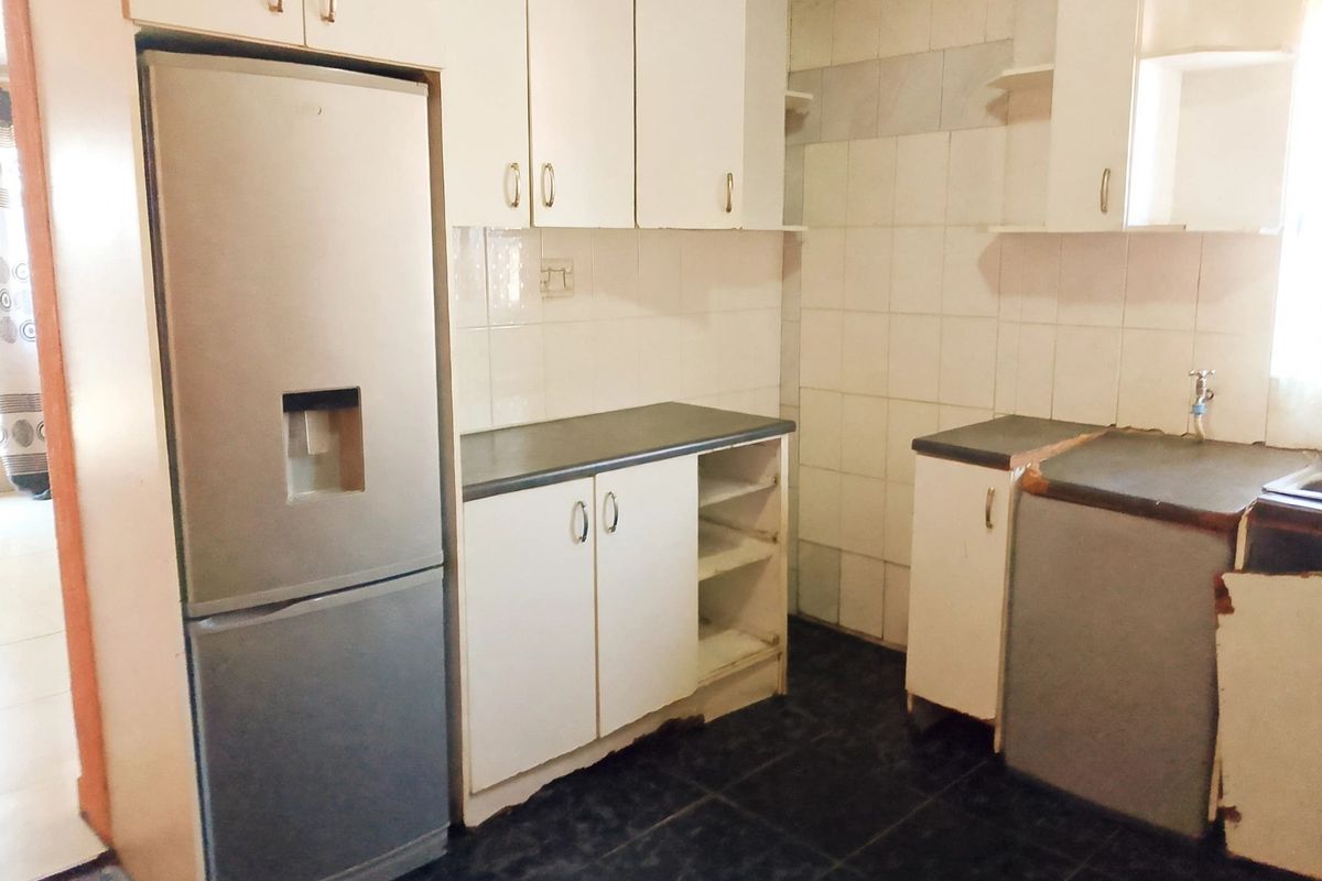A functional kitchen featuring white cabinetry, dark laminate countertops, tiled backsplash, and dark floor tiles, showing signs of wear and requiring cosmetic updates.