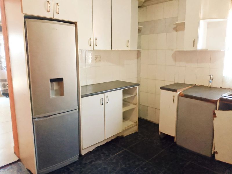 A functional kitchen featuring white cabinetry, dark laminate countertops, tiled backsplash, and dark floor tiles, showing signs of wear and requiring cosmetic updates.