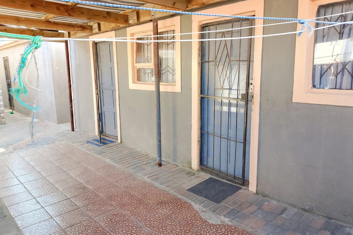 A covered rear patio area featuring paved flooring, timber roof structure, and multiple access points with security gates.
