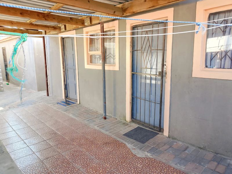 A covered rear patio area featuring paved flooring, timber roof structure, and multiple access points with security gates.