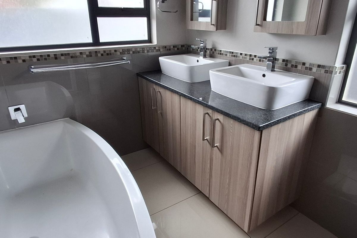 Modern bathroom featuring a double vanity with vessel sinks, granite countertop, built-in cabinetry, and a sleek freestanding bathtub with tiled finishes.