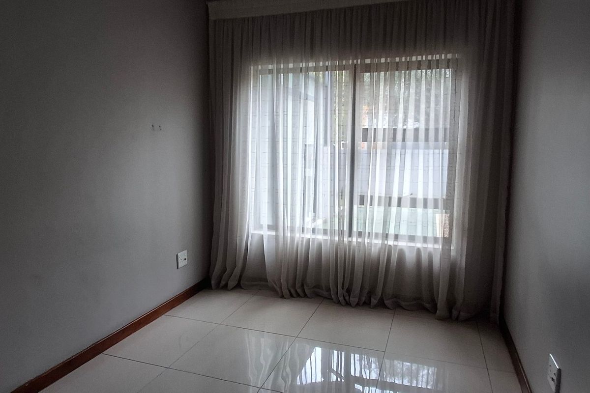 A bright, empty bedroom featuring neutral tiled flooring, clean wall finishes, and large windows dressed with floor-to-ceiling curtains.