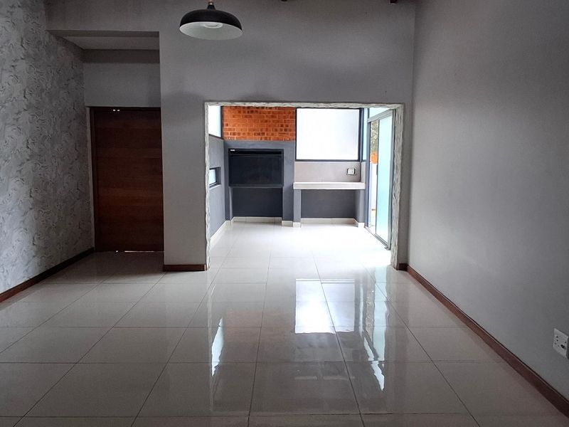 Spacious open-plan living area featuring polished tile flooring, a textured feature wall, and a built-in braai area with direct access to the outdoors.