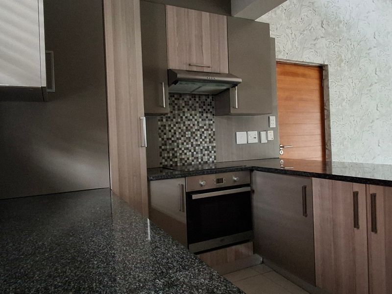 Modern kitchen featuring granite countertops, built-in oven, extractor fan, and ample cabinetry, finished with a mosaic tile backsplash and neutral tiled flooring.