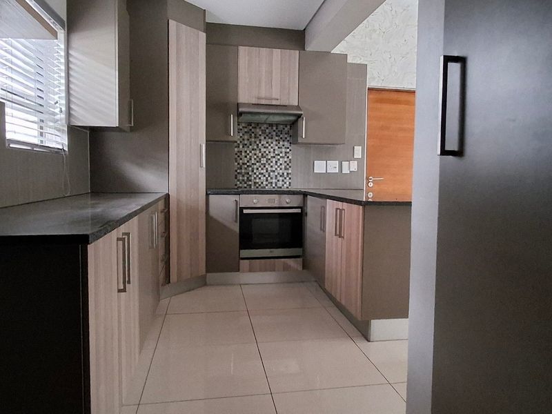 Modern kitchen featuring sleek built-in cabinetry, stone countertops, a mosaic tile backsplash, and integrated oven with extractor fan.