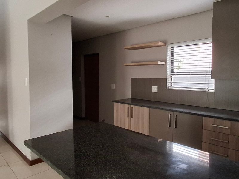Modern kitchen featuring sleek built-in cabinetry, stone countertops, a functional island, and floating shelves, creating a clean and contemporary culinary space.
