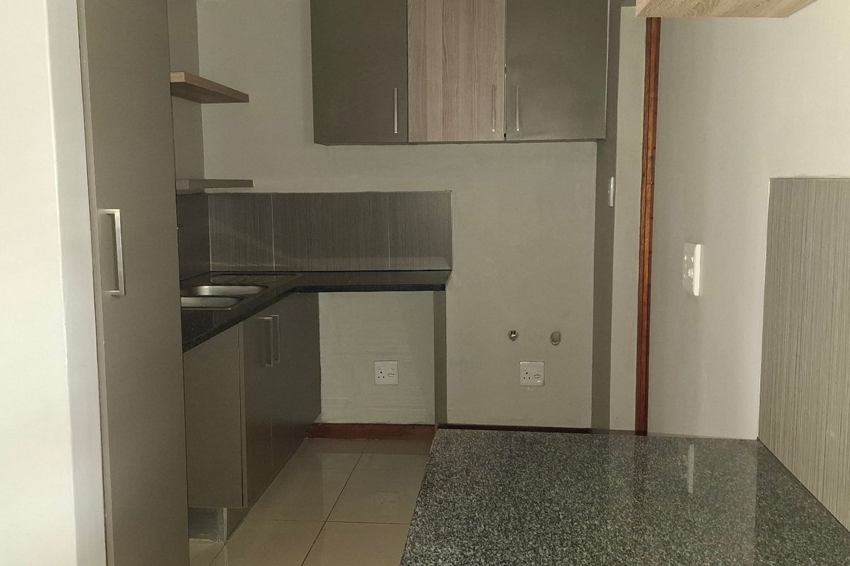 A clean, modern kitchen featuring granite countertops, ample built-in cabinetry, a double sink, and tiled finishes throughout.