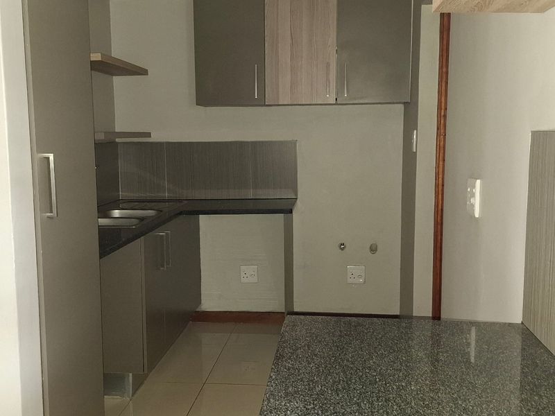 A clean, modern kitchen featuring granite countertops, ample built-in cabinetry, a double sink, and tiled finishes throughout.