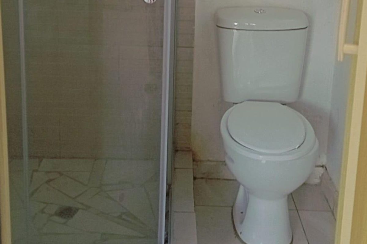 A compact bathroom featuring a shower enclosure and a standard toilet, requiring some maintenance and cosmetic updates to the tiling and wall finishes.