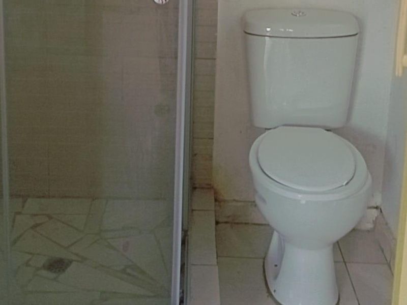 A compact bathroom featuring a shower enclosure and a standard toilet, requiring some maintenance and cosmetic updates to the tiling and wall finishes.