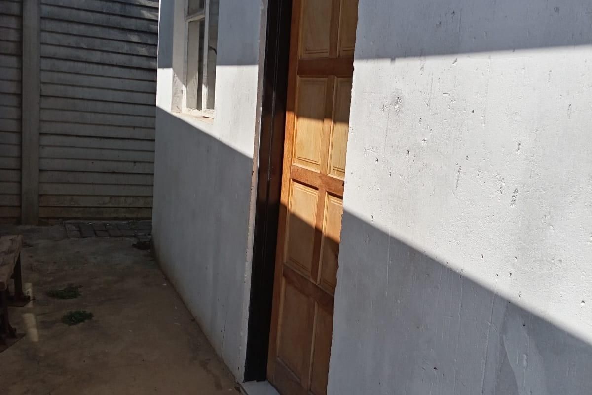 A view of the rear exterior area featuring a timber panel door, concrete paving, and a precast concrete boundary wall.