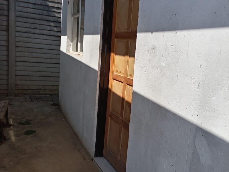 A view of the rear exterior area featuring a timber panel door, concrete paving, and a precast concrete boundary wall.