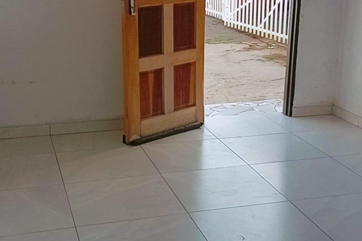 An empty entrance area featuring light-colored floor tiles and a wooden door leading to an outdoor space.
