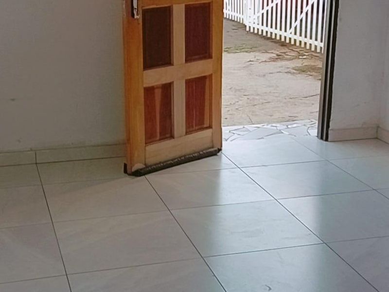 An empty entrance area featuring light-colored floor tiles and a wooden door leading to an outdoor space.