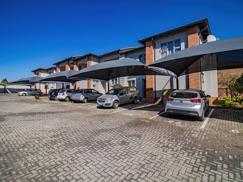 Exterior view of the apartment complex featuring a paved parking area with dedicated shade cloth carports for residents.