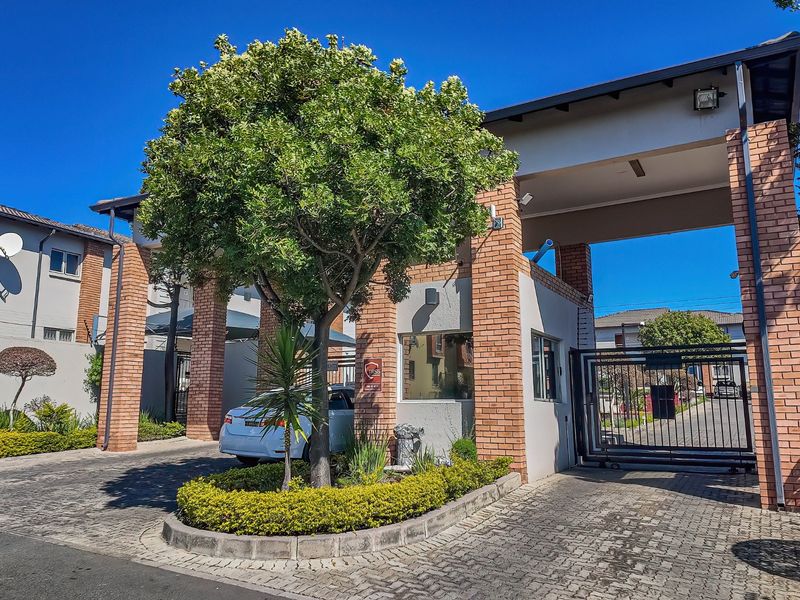 The secure entrance to the apartment complex features brick pillars, a guard house, and a gated driveway with paved access.