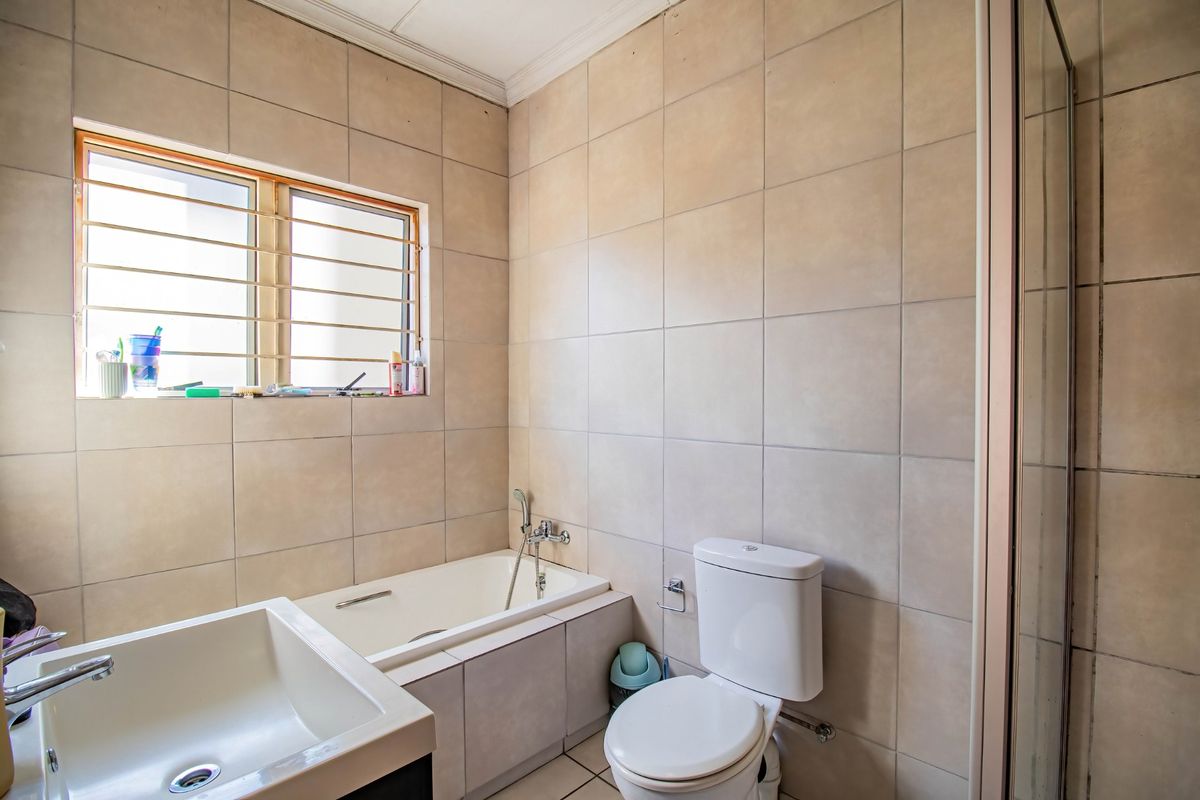 A functional bathroom featuring a bathtub, separate shower enclosure, toilet, and vanity basin with neutral wall tiling and security bars on the window.