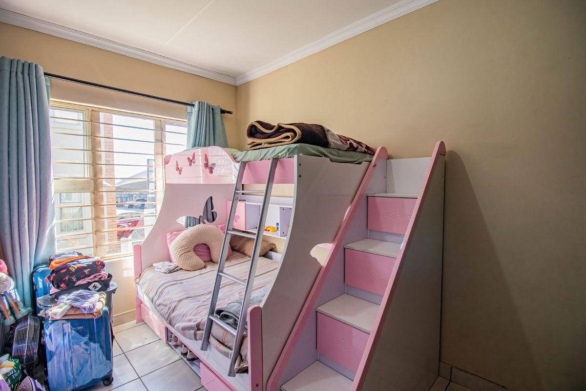 A bedroom featuring tiled flooring and security bars on the window, providing a functional space with natural light.
