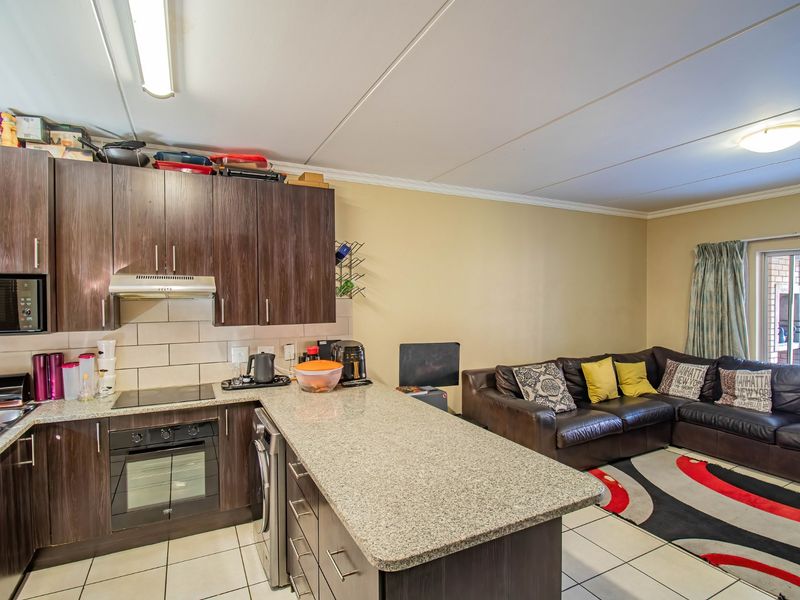 Open-plan living area featuring a kitchen with dark wood cabinetry, granite countertops, and integrated appliances, flowing into a comfortable lounge space with tiled flooring.