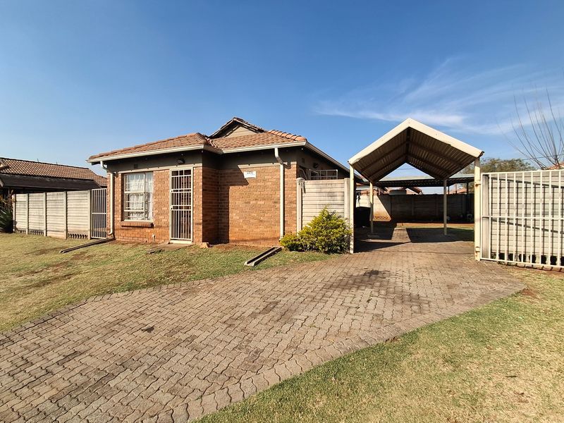 Front view of a brick house featuring a paved driveway, a covered carport, and secure boundary walling.