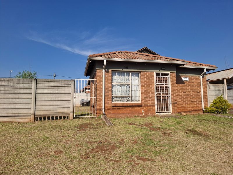 Front view of a face brick house featuring a tiled roof, security gate, and precast concrete boundary wall on a grassed plot.