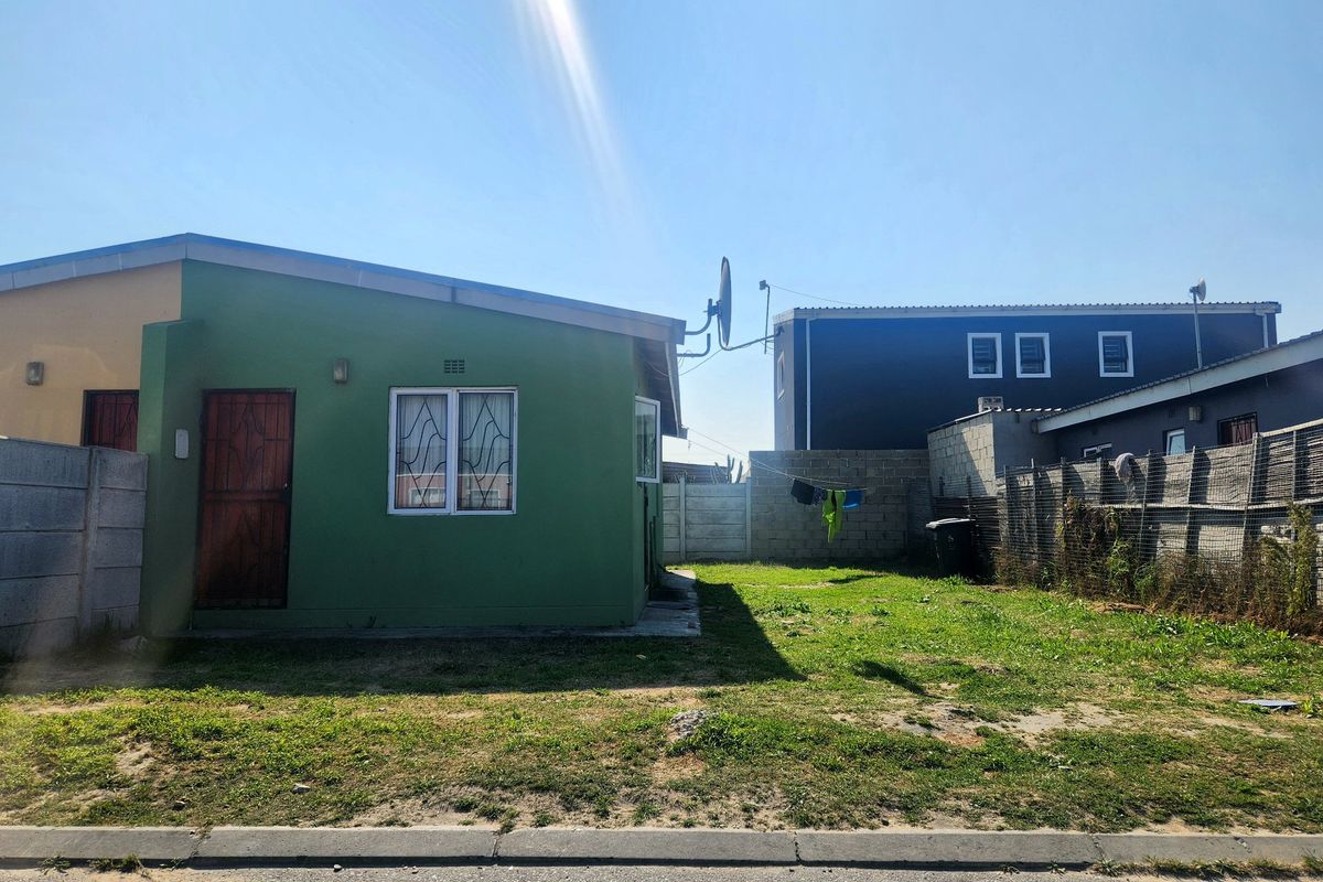 Rear view of the property featuring a private garden area, concrete boundary walls, and a secure exterior entrance.
