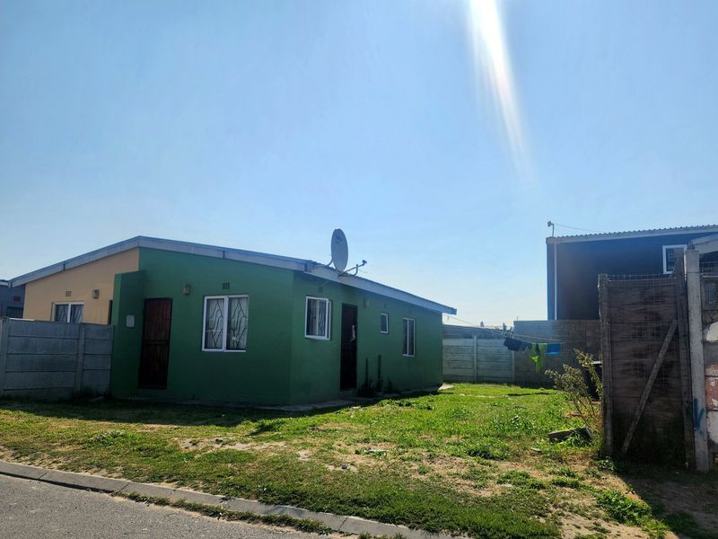 A detached single-story house featuring a green exterior facade, security gates, and a surrounding precast concrete boundary wall with an open yard area.