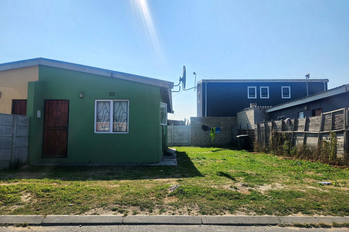 Rear view of the property featuring a green exterior wall, security gates, and a fenced backyard area with lawn.