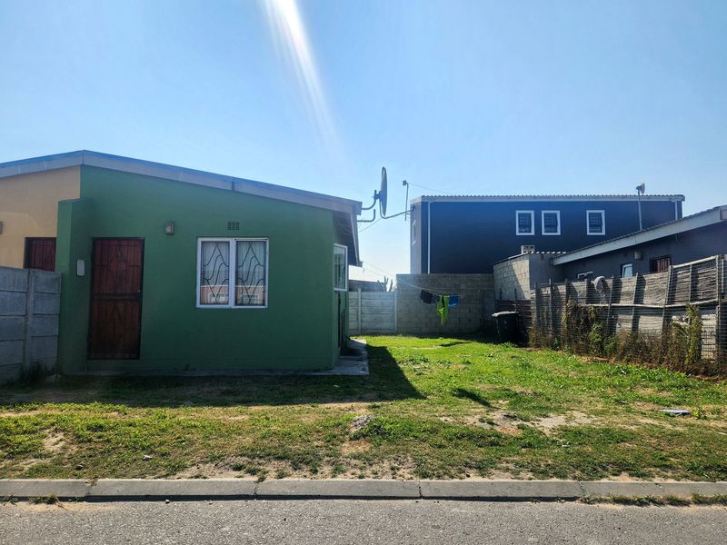 Rear view of the property featuring a green exterior wall, security gates, and a fenced backyard area with lawn.