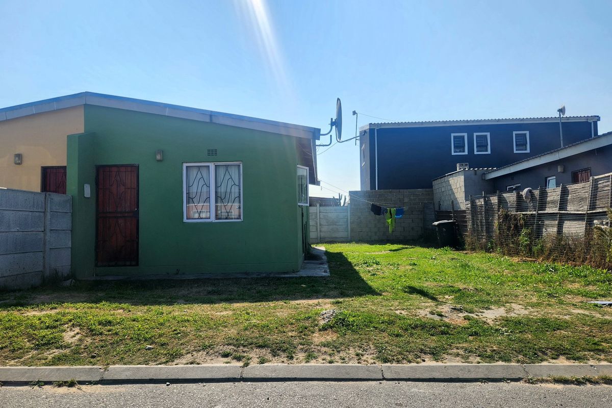Front view of a single-story house featuring a green facade, security gate, and a fenced yard area.