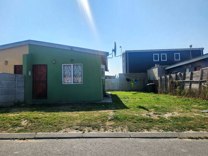 Front view of a single-story house featuring a green facade, security gate, and a fenced yard area.