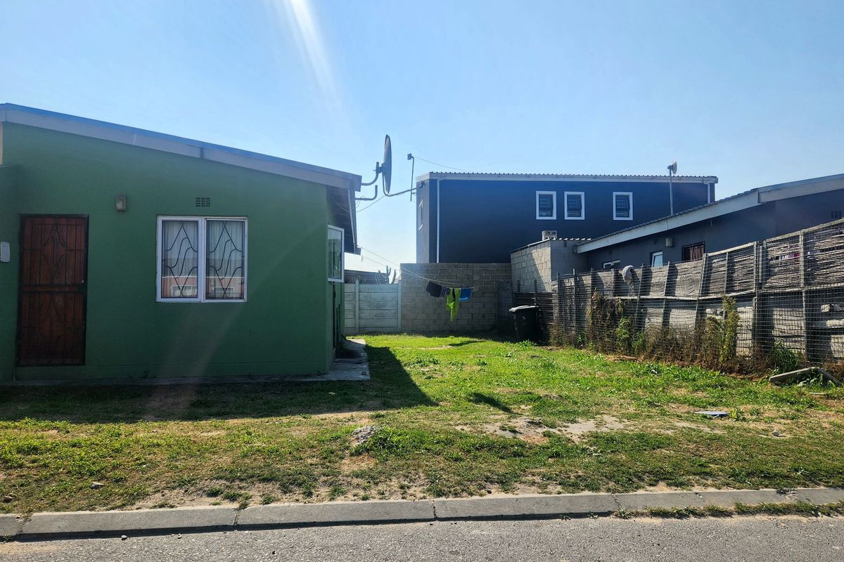 Rear exterior view of the property featuring a green facade, security features, and a fenced backyard area.