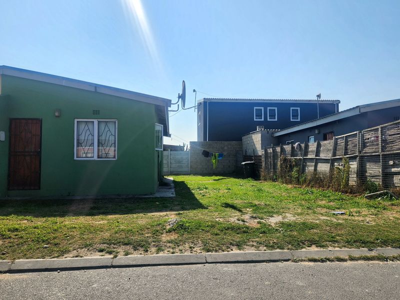 Rear exterior view of the property featuring a green facade, security features, and a fenced backyard area.