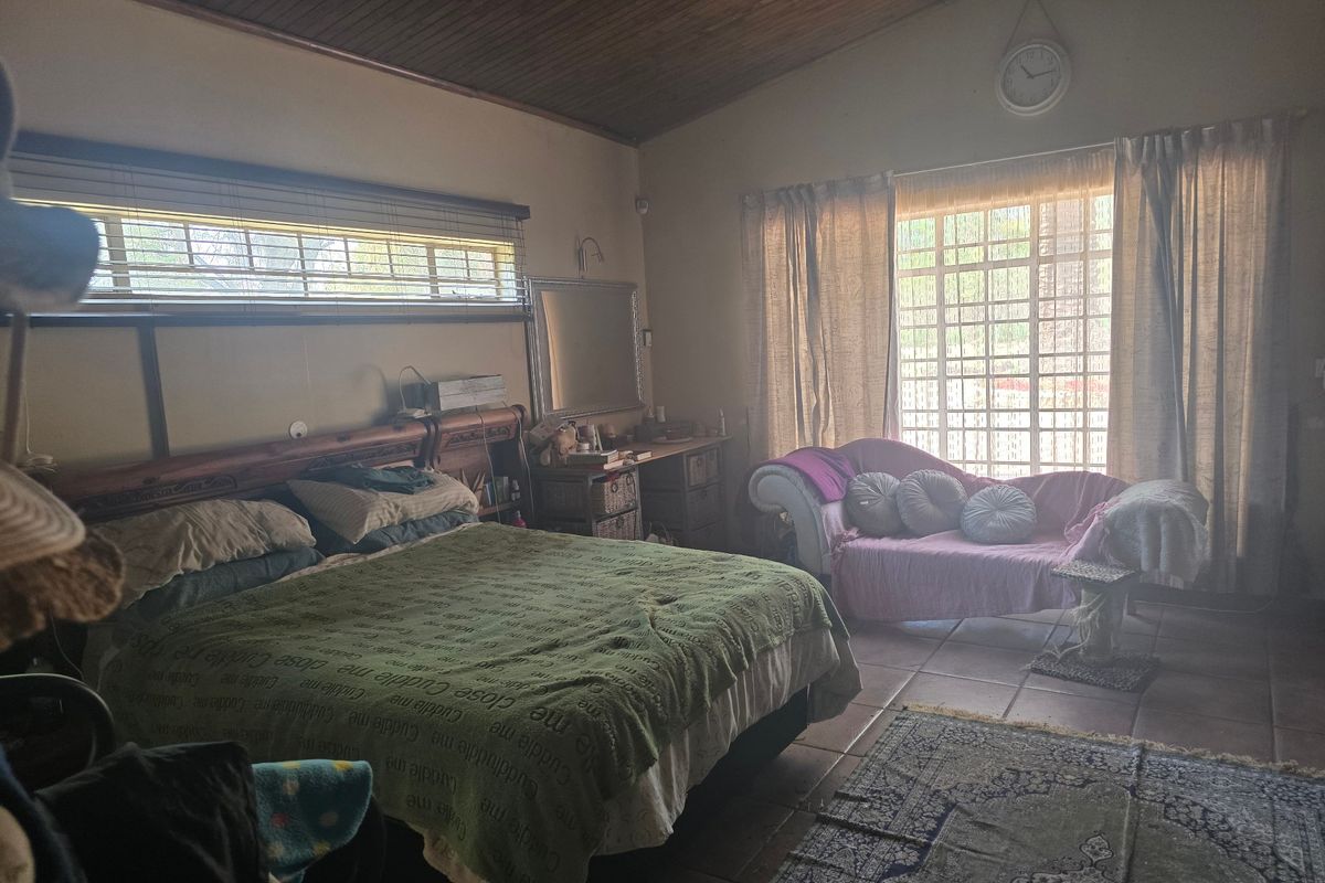 A spacious bedroom featuring a timber-clad ceiling, tiled flooring, and large windows with security bars, offering a functional layout with natural light.