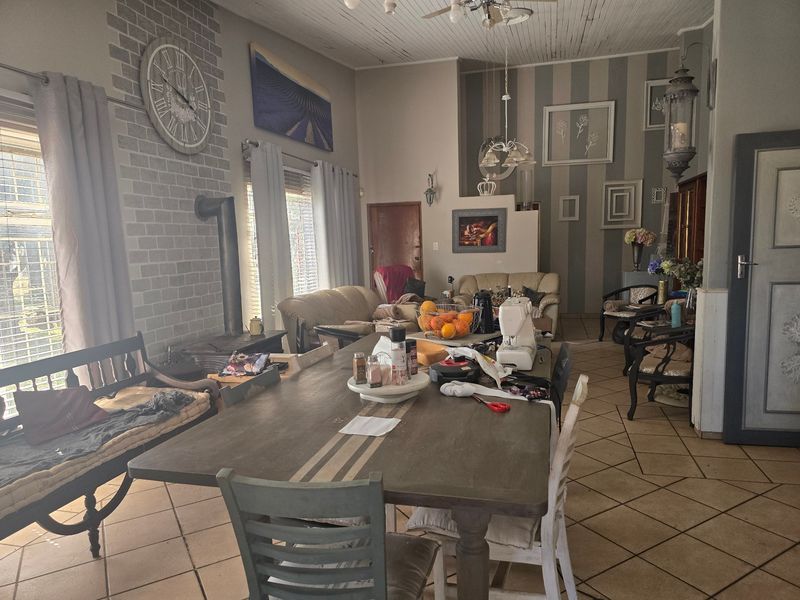 Spacious open-plan living and dining area featuring a wood-burning stove, brick accent wall, and tiled flooring with high ceilings.