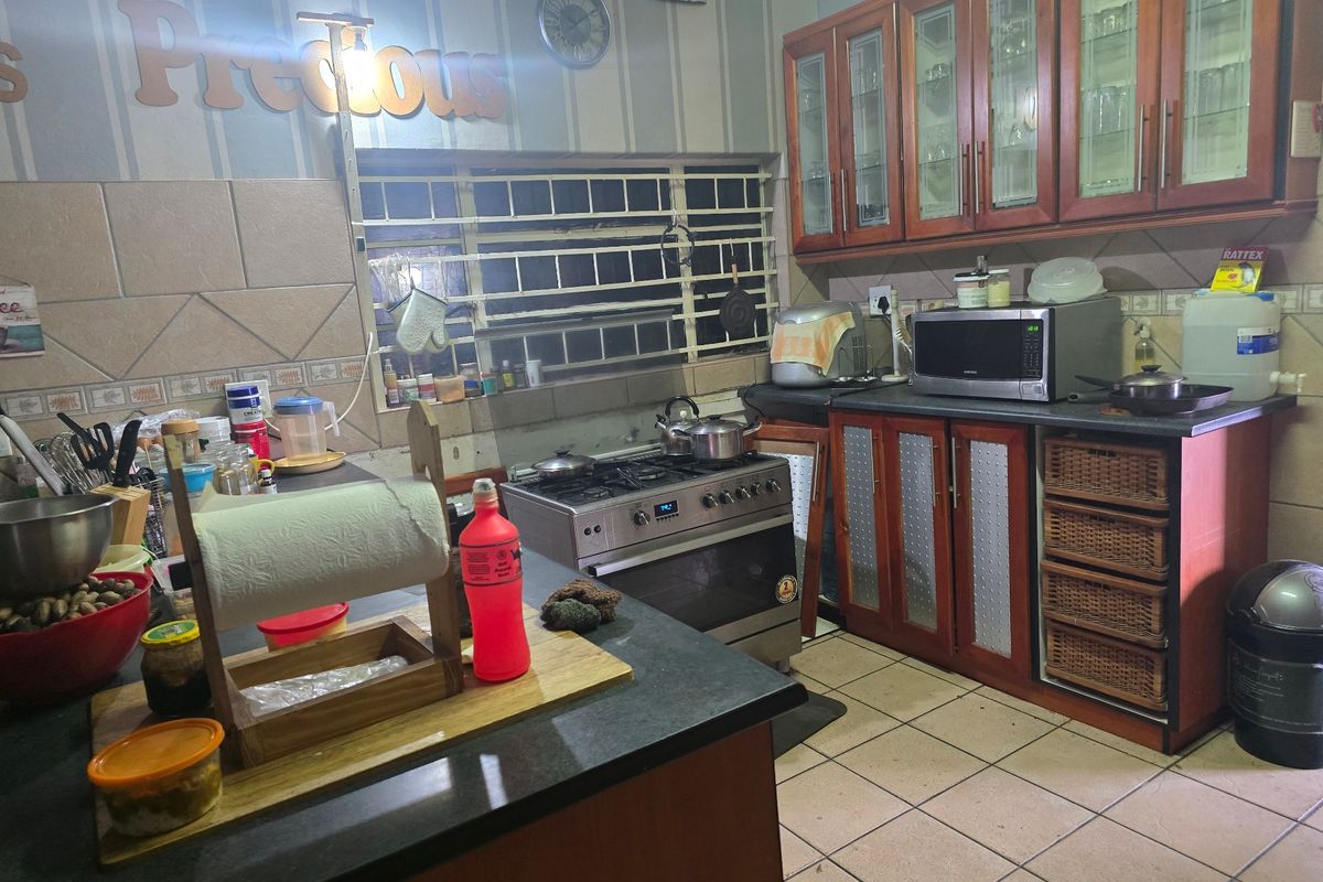 A functional kitchen featuring wooden cabinetry, a gas stove with oven, tiled flooring, and a tiled backsplash with security bars on the window.