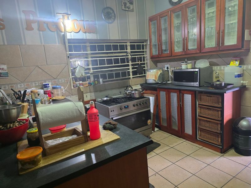 A functional kitchen featuring wooden cabinetry, a gas stove with oven, tiled flooring, and a tiled backsplash with security bars on the window.