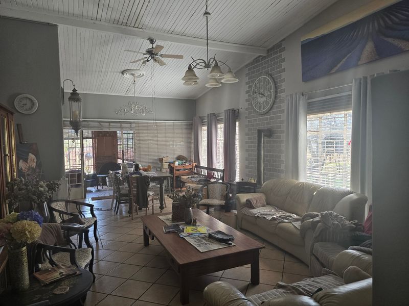 Spacious open-plan living area featuring a brick fireplace, exposed beam ceiling, tiled floors, and direct access to an outdoor patio area.